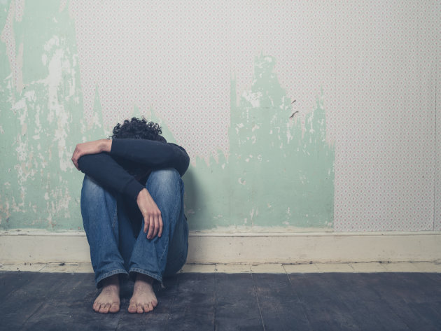 A sad and depressed young man is sitting on the floor in an empty room