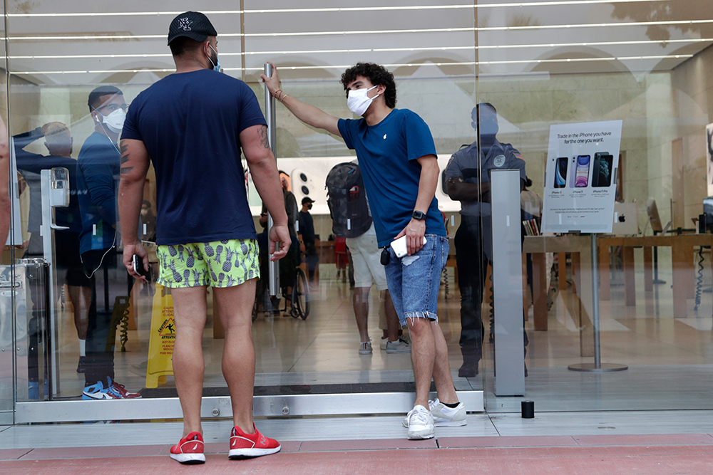 An employee wearing a protective face covering, right, monitors the flow of customers at an Apple retail store along Lincoln Road Mall during the new coronavirus pandemic, Wednesday, June 17, 2020, in Miami Beach, Fla. (AP Photo/Lynne Sladky)